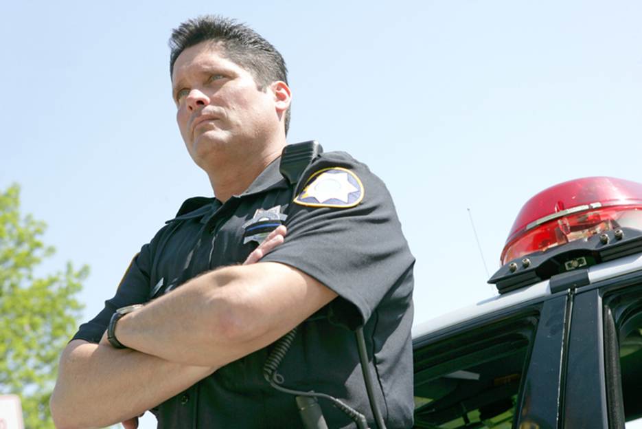 An officer in uniform stands with his arms crossed next to a police car. The image accompanies content about legal protections for minors.